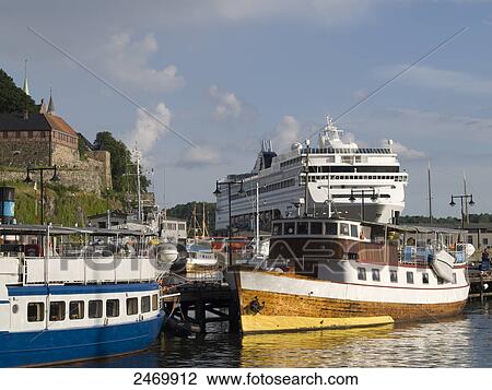 Stock Image - Boats docked at harbor with fort in background, Akershus fortress, Oslo, Norway . Fotosearch