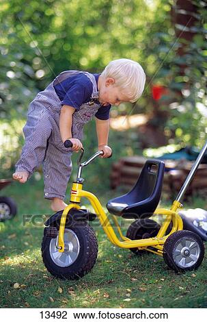 Stock Image - Boy climbing upon a tricycle . Fotosearch