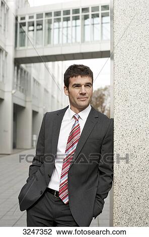 Stock Image - Businessman leaning against wall, three quarter length . Fotosearch