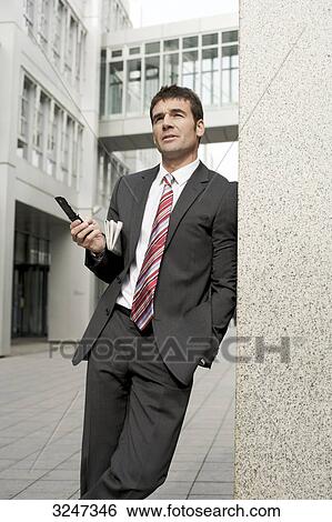 Stock Photograph - Businessman leaning against wall, three quarter length . Fotosearch