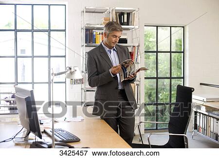 Businessman reading a magazine in an office View Large Photo Image Stock Photo - Businessman reading a magazine in an office . Fotosearch