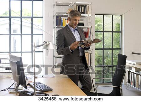 Businessman reading a magazine in an office View Large Photo Image Stock Photo - Businessman reading a magazine in an office . Fotosearch