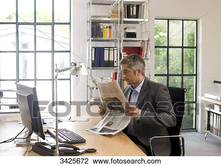 Businessman reading a newspaper at his desk View Large Photo Image Stock Image - Businessman reading a newspaper at his desk . Fotosearch