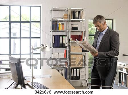 Stock Photograph - Businessman reading a newspaper in an office . Fotosearch