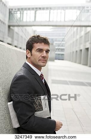 Businessman with newspaper leaning against wall, waist up View Large Photo Image Stock Photo - Businessman with newspaper leaning against wall, waist up . Fotosearch