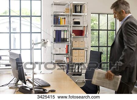 Businessman with newspaper standing in front of his desk View Large Photo Image Stock Photography - Businessman with newspaper standing in front of his desk . Fotosearch