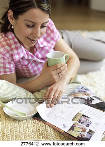 Stock Image - Close-up of woman reading magazine and holding coffee cup . Fotosearch