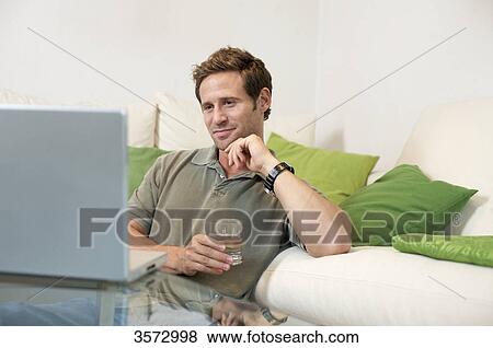 Stock Photo - Content man in living room looking at laptop . Fotosearch