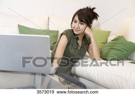 Stock Photo - Content woman in living room looking at laptop . Fotosearch