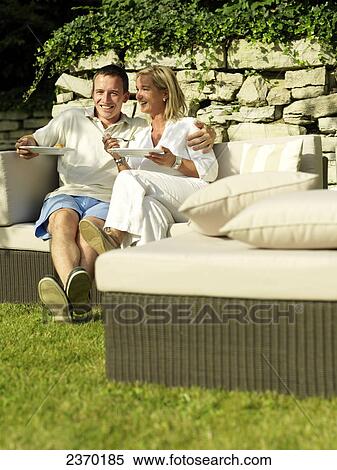 Stock Photography - Couple eating food and smiling on couch . Fotosearch