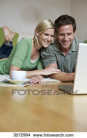 Couple lying on floor and looking at laptop View Large Photo Image Picture - Couple lying on floor and looking at laptop . Fotosearch