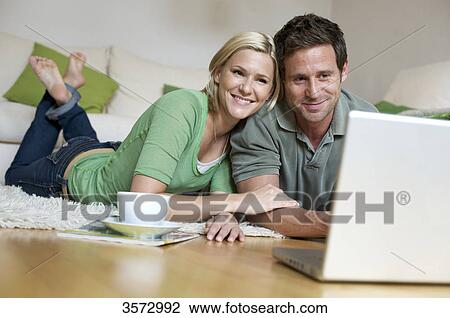 Couple lying on floor and looking at laptop View Large Photo Image Stock Image - Couple lying on floor and looking at laptop . Fotosearch
