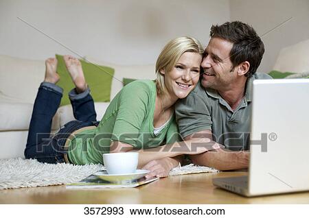 Stock Image - Couple lying on floor and looking at laptop . Fotosearch