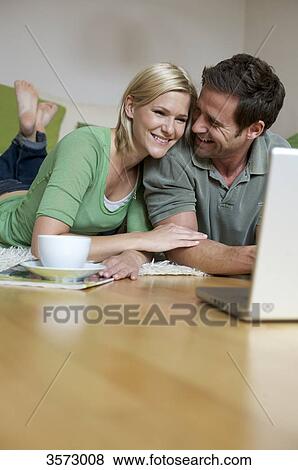 Stock Photo - Couple lying on floor and looking at laptop . Fotosearch