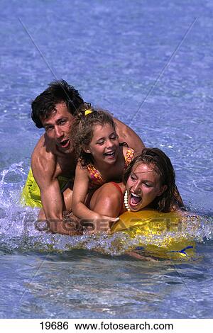 Stock Photograph - Family lying on an inflatable fish in water . Fotosearch