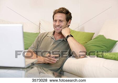 Stock Photo - Happy man in living room looking at laptop . Fotosearch