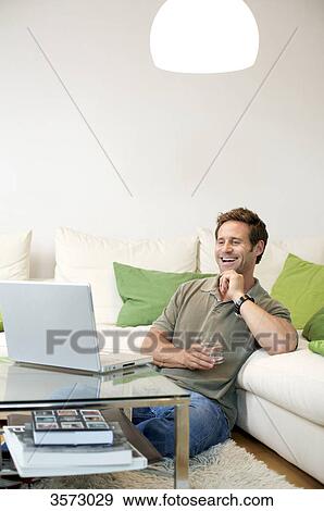 Stock Photo - Happy man in living room looking at laptop . Fotosearch