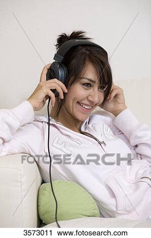 Stock Image - Happy woman in living room wearing headphones . Fotosearch