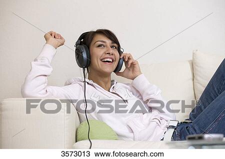 Stock Image - Happy woman in living room wearing headphones . Fotosearch