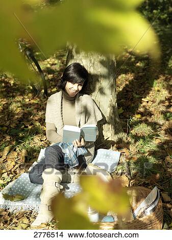 Picture - High angle view of mature woman reading book under shadow of tree . Fotosearch