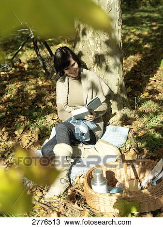 Stock Image - High angle view of mature woman reading book under shadow of tree . Fotosearch