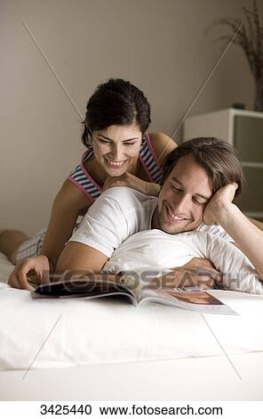 Stock Image - Man and woman reading a magazine on bed, low angle view . Fotosearch