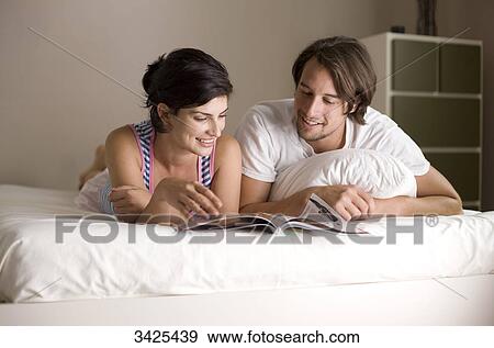 Man and woman reading a magazine on bed, low angle view View Large Photo Image Stock Photo - Man and woman reading a magazine on bed, low angle view . Fotosearch