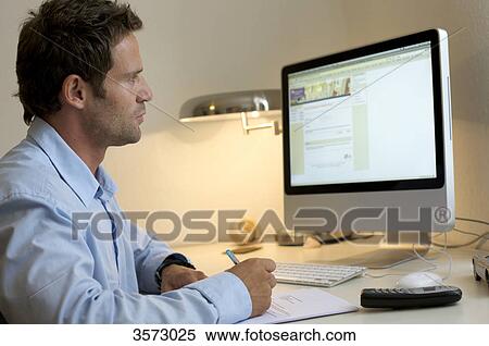 Man at desk looking at monitor and writing View Large Photo Image Stock Photography - Man at desk looking at monitor and writing . Fotosearch