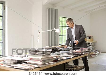 Man looking at magazines and books on a table View Large Photo Image Picture - Man looking at magazines and books on a table . Fotosearch