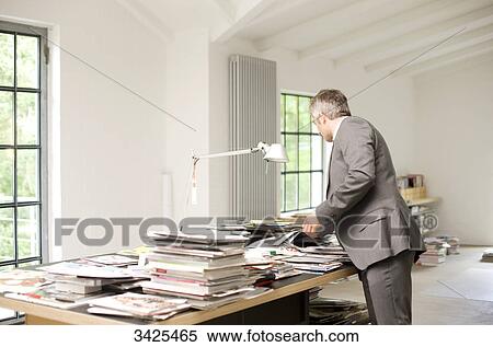 Stock Photography - Man looking at magazines and books on a table . Fotosearch