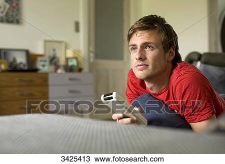 Man lying on a couch, holding a remote control View Large Photo Image Stock Image - Man lying on a couch, holding a remote control . Fotosearch