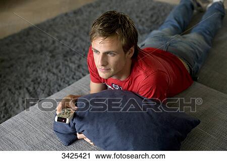 Man lying on a couch, holding a remote control, elevated view View Large Photo Image Stock Image - Man lying on a couch, holding a remote control, elevated view . Fotosearch