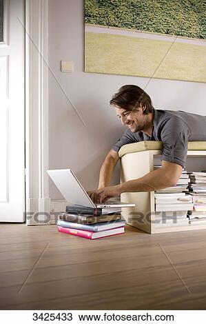 Stock Image - Man lying on a shelf and using a notebook, low angle view . Fotosearch