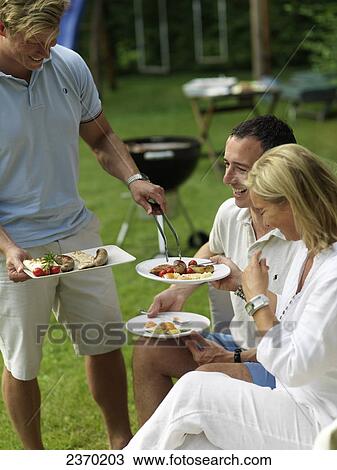 Stock Image - Man serving food to his friends at a garden party . Fotosearch