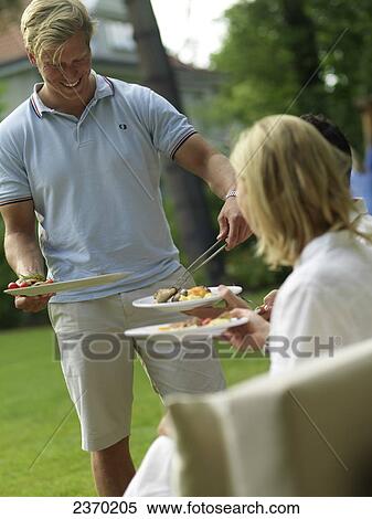 Stock Photography - Man serving food to his friends at a garden party . Fotosearch