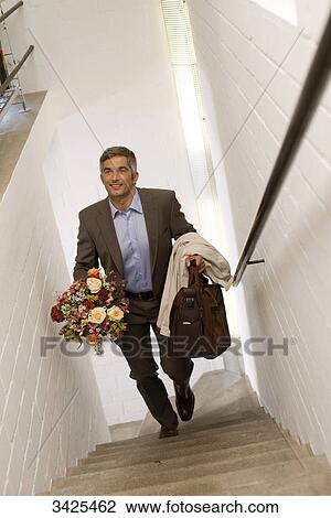 Stock Image - Man with a bouquet and bag walking upstairs, elevated view . Fotosearch