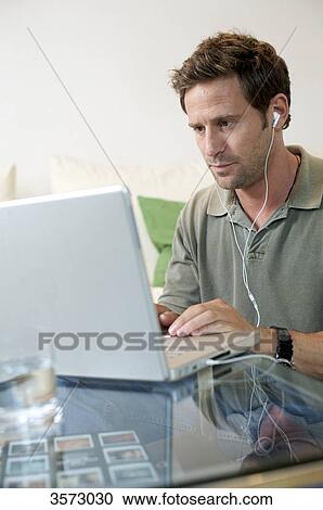 Man with earbuds using laptop View Large Photo Image Stock Image - Man with earbuds using laptop . Fotosearch
