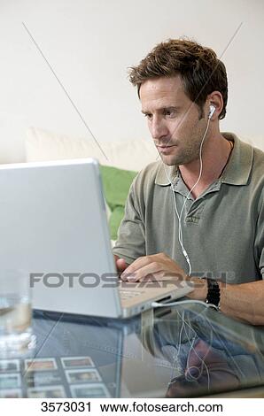 Stock Image - Man with earbuds using laptop . Fotosearch