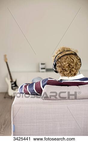 Man with headphones sitting on a couch, e-guitar in the background, rear view View Large Photo Image Stock Image - Man with headphones sitting on a couch, e-guitar in the background, rear view . Fotosearch
