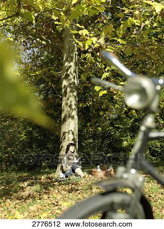 Stock Image - Mature woman leaning against tree in park . Fotosearch