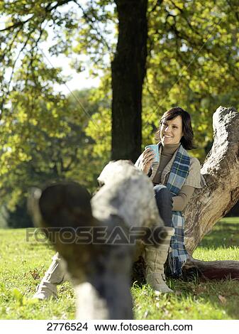 Mature woman sitting on fallen tree and smiling View Large Photo Image Picture - Mature woman sitting on fallen tree and smiling . Fotosearch