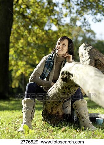Mature woman sitting on fallen tree and smiling View Large Photo Image Stock Photo - Mature woman sitting on fallen tree and smiling . Fotosearch