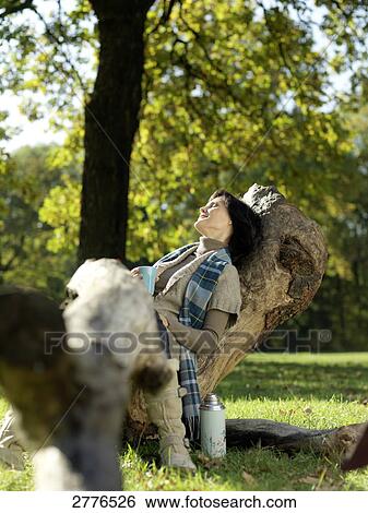 Stock Photograph - Mature woman sitting on fallen tree and smiling . Fotosearch