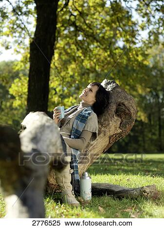 Stock Photography - Mature woman sitting on fallen tree and smiling . Fotosearch