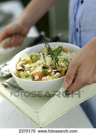 Stock Image - Mid section view of woman holding bowl of pasta salad on tray . Fotosearch