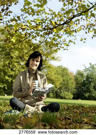 Stock Photo - Portrait of mature woman holding book and smiling in park . Fotosearch