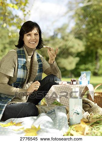 Stock Photography - Portrait of mature woman holding slice of bread and smiling in park . Fotosearch