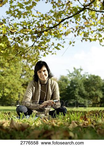 Stock Photo - Portrait of mature woman listening to mp3 player in park . Fotosearch