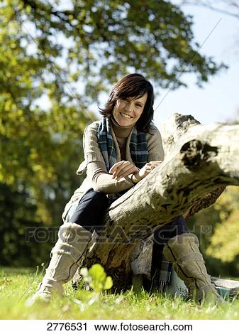 Portrait of mature woman sitting on fallen tree and smiling View Large Photo Image Stock Image - Portrait of mature woman sitting on fallen tree and smiling . Fotosearch