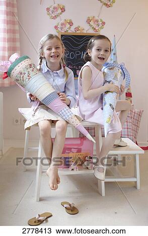 Portrait of two girls holding cardboard cones and smiling on table View Large Photo Image Stock Image - Portrait of two girls holding cardboard cones and smiling on table . Fotosearch
